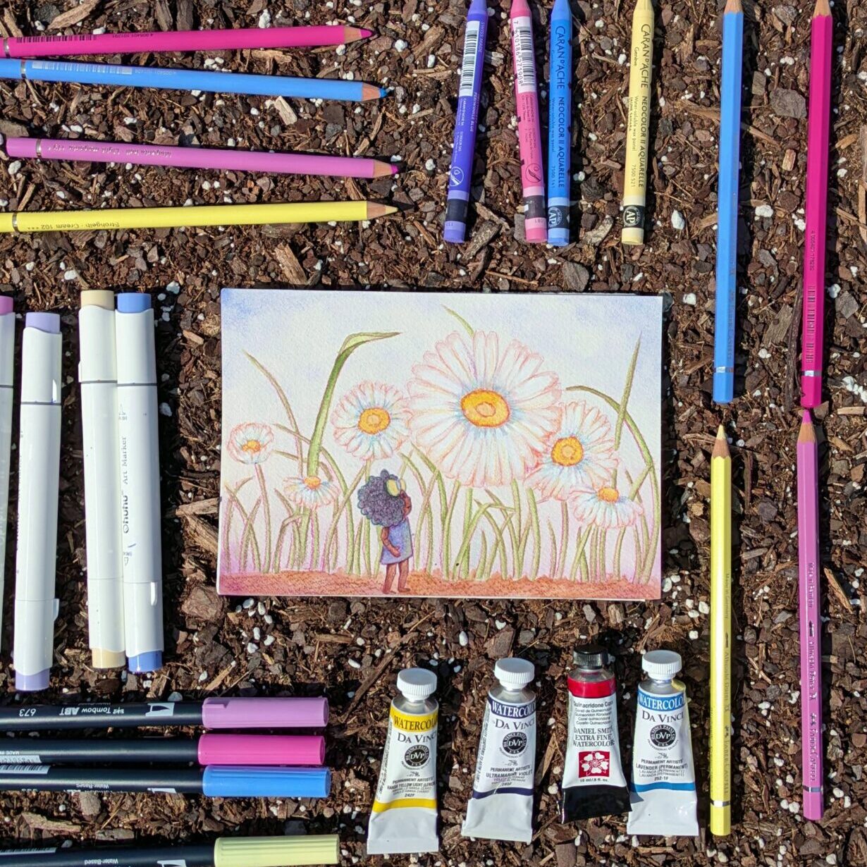 A painting of a little girl surrounded by giant daisies lays on the dirt in a rise bed garden surrounded by pale yellow, light pink, lavender and periwinkle art supplies.