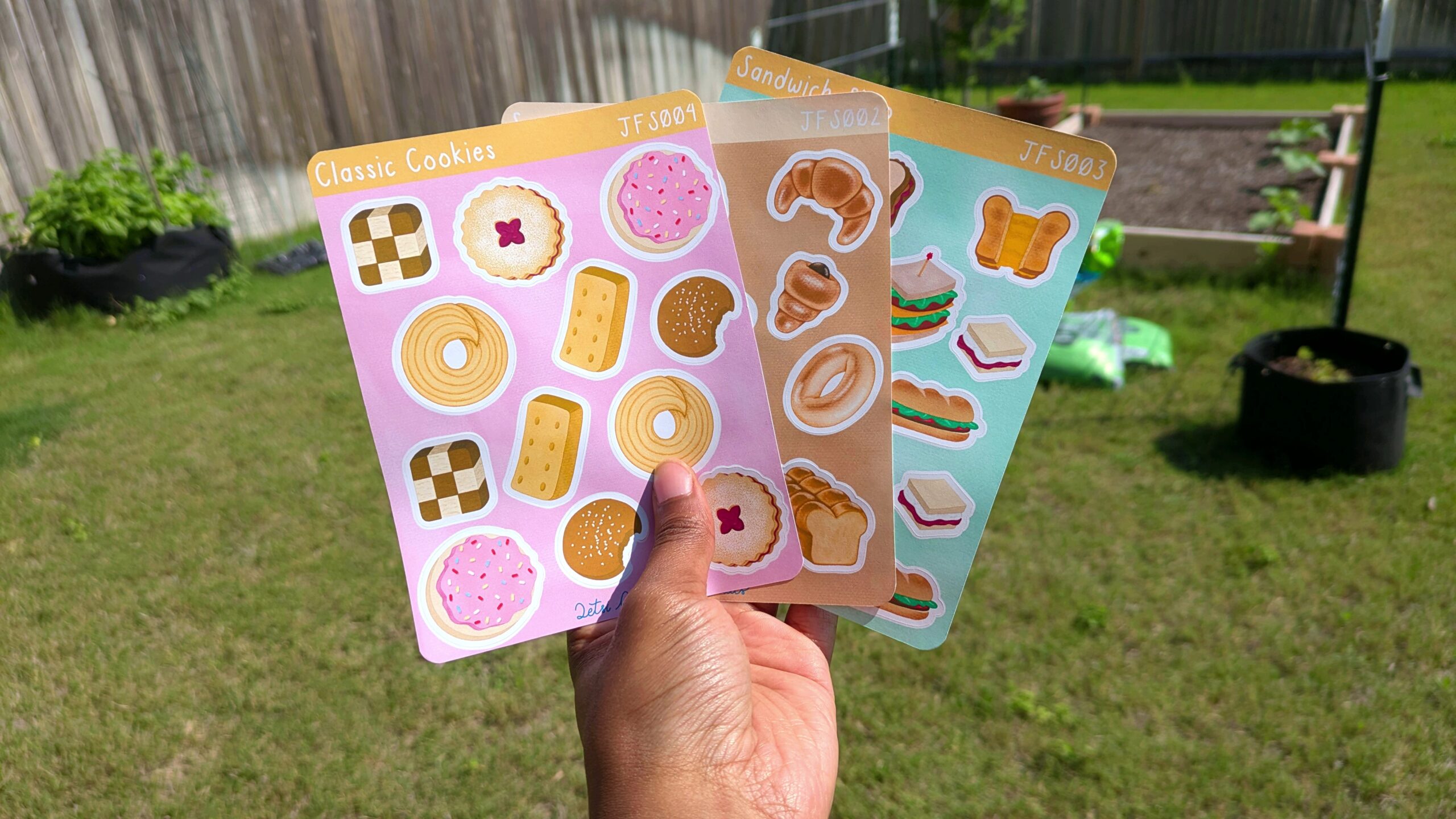 A hand holds 3 sticker sheets from Qetsi Creates Shop